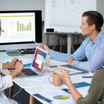 Three individuals work together at a table with a laptop and whiteboard, focused on enhancing leads for a Dallas PPC firm.