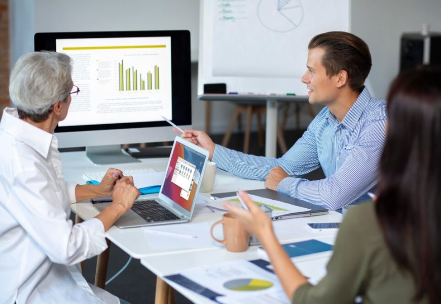 Three individuals work together at a table with a laptop and whiteboard, focused on enhancing leads for a Dallas PPC firm.