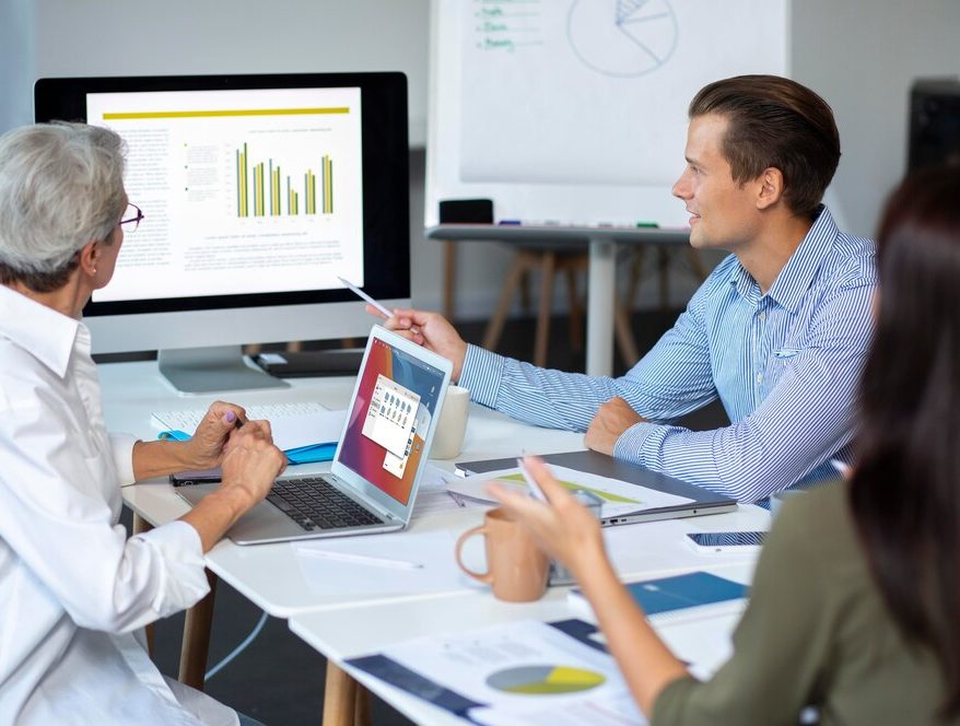 Three individuals work together at a table with a laptop and whiteboard, focused on enhancing leads for a Dallas PPC firm.